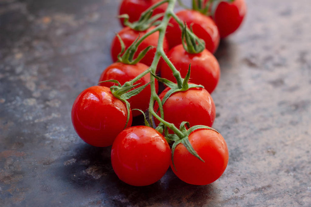 Fresh organic bright small red cherry tomatoes with green branch on dark brown and black rustic metal background - 写真・画像