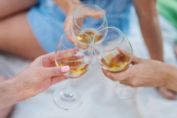 Tři ženské ruce s brýlemi z bílého vína. Přípitek, gratuluji k venkovnímu pikniku. Koncept relaxace a přátelství. - Fotografie, Obrázek