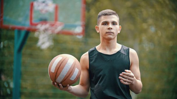Młody człowiek Fit stoi na boisko sportowe i trzyma piłkę do koszykówki - Zdjęcie, obraz