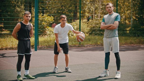 Tre sportivi in piedi sul campo da basket all'aperto e guardando nella fotocamera
 - Foto, immagini