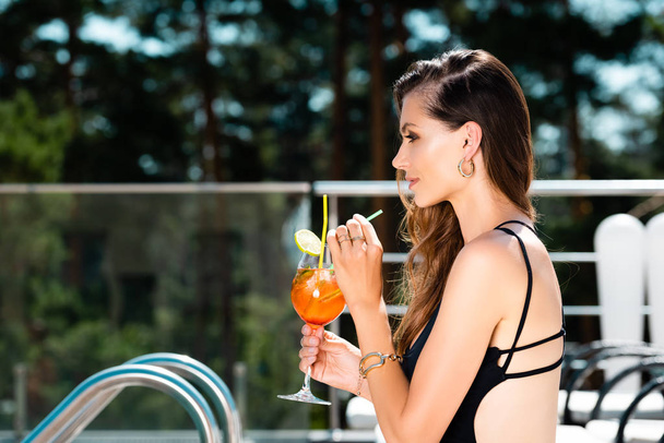 vista lateral de mujer atractiva en traje de baño con cóctel en el resort
 - Foto, Imagen