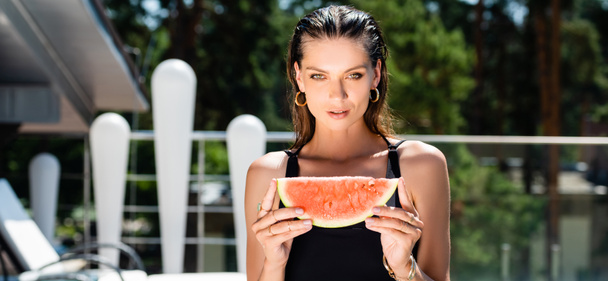 Panoramaaufnahme einer schönen Frau im Badeanzug, die mit Wassermelone im Resort posiert - Foto, Bild