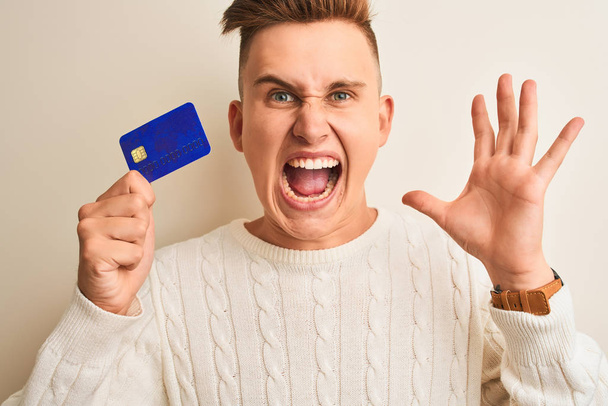 Young handsome man holding credit card over isolated white background very happy and excited, winner expression celebrating victory screaming with big smile and raised hands - Fotografie, Obrázek