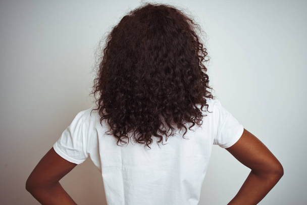 Jonge Afro-Amerikaanse vrouw dragen t-shirt staande over geïsoleerde witte achtergrond staande achteruit kijken weg met armen op lichaam - Foto, afbeelding