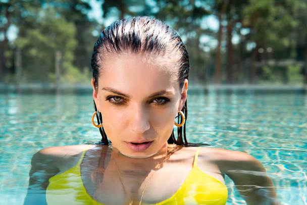 beautiful sexy woman in swimwear in pool looking at camera on resort - Foto, afbeelding