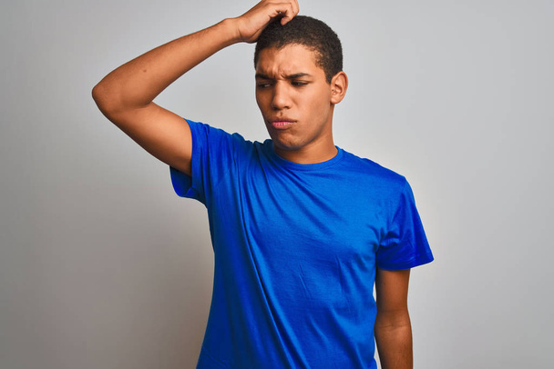 Jeune homme arabe beau portant t-shirt bleu debout sur fond blanc isolé confondre et s'interroger sur la question. Incertain avec le doute, pensant la main sur la tête. Concept pensif
. - Photo, image