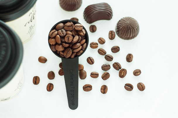 Καραμέλες μαύρης σοκολάτας, γλυκά με μια κουταλιά φασόλια καφέ σε ανοιχτόχρωμο φόντο. Έννοια του τρόπου ζωής. - Φωτογραφία, εικόνα
