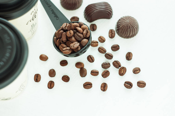 Тёмные шоколадные конфеты, сладости с ложкой кофейных зерен на светлом фоне. Концепция образа жизни
. - Фото, изображение