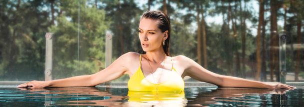 panoramic shot of beautiful sexy woman in swimming suit posing in pool on resort - Photo, Image