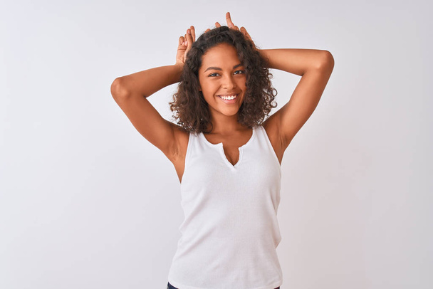 Young brazilian woman wearing casual t-shirt standing over isolated white background Posing funny and crazy with fingers on head as bunny ears, smiling cheerful - Foto, afbeelding