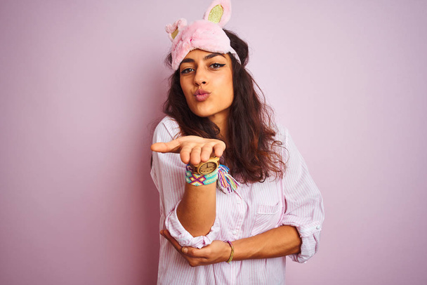 Young beautiful woman wearing pajama and sleep mask over isolated pink background looking at the camera blowing a kiss with hand on air being lovely and sexy. Love expression. - Photo, Image