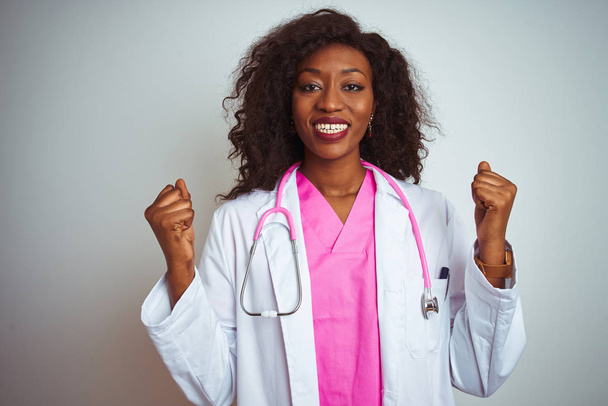 Africká americká doktorka, Žena s růžovým stetoskem nad izolovaným bílým pozadím, oslavovala překvapení a žasla nad úspěchem se zdviženýma rukama a otevřenými zraky. Koncepce vítězů. - Fotografie, Obrázek