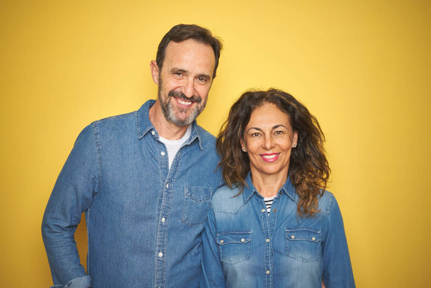 Bella coppia di mezza età insieme in piedi su sfondo giallo isolato con un sorriso felice e fresco sul viso. Persona fortunato
. - Foto, immagini