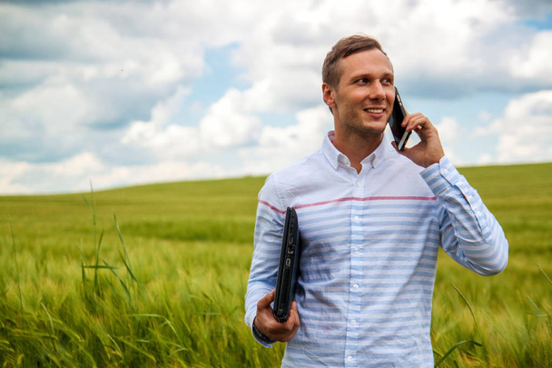 hombre de negocios con computadora portátil y teléfono inteligente en el campo de trigo
. - Foto, Imagen