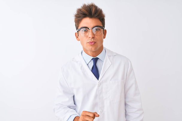 Der junge, gut aussehende Wissenschaftler mit Brille und Mantel vor isoliertem weißem Hintergrund, der in die Kamera blickt und einen Kuss in die Luft bläst, ist schön und sexy. Liebesausdruck. - Foto, Bild