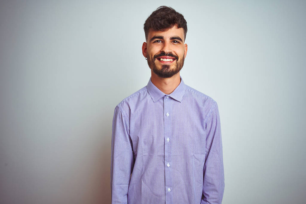 Fiatal férfi tetoválás viselt lila inget állva elszigetelt fehér háttér egy boldog és hűvös mosoly az arcon. Szerencsés ember. - Fotó, kép