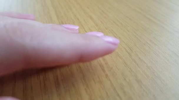 白い肌とピンクの短いマニキュアを持つ女性の手は、木製のテーブルのクローズアップに爪と指でノック - 映像、動画