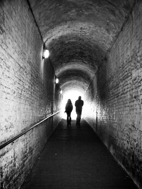 alter dunkler Fußgängertunnel mit zwei Personen in Silhouette gegen weißes Licht, das vorwärts geht - Foto, Bild