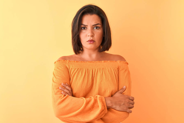 孤立したオレンジ色の背景に立つカジュアルなTシャツを着た若い美しい女性は懐疑的で神経質で、腕を組んだ顔に失望した表情を浮かべていた。否定的な人. - 写真・画像