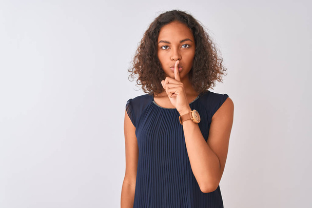 Giovane donna brasiliana indossa abito blu in piedi sopra isolato sfondo bianco chiedendo di essere tranquillo con il dito sulle labbra. Silenzio e concetto segreto
. - Foto, immagini
