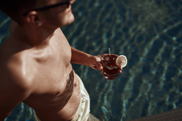 Cropped photo of young muscular guy keeping glass with beverage in hand - Фото, изображение