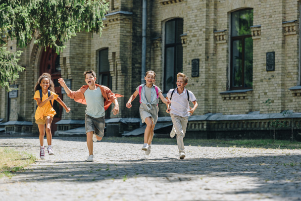 quattro adorabili scolari multiculturali sorridenti mentre corrono nel cortile della scuola
 - Foto, immagini
