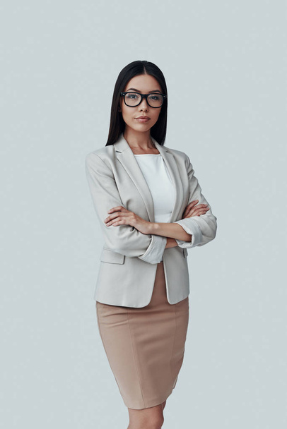 Intelligenz. attraktive junge asiatische Frau blickt in die Kamera und lächelt vor grauem Hintergrund - Foto, Bild