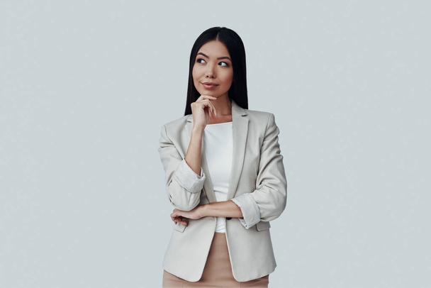 What if... Attractive young Asian woman looking away and smiling while standing against grey background - Фото, изображение