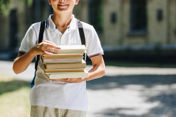 vista ritagliata di scolaro sorridente con zaino che tiene libri nel cortile della scuola
 - Foto, immagini