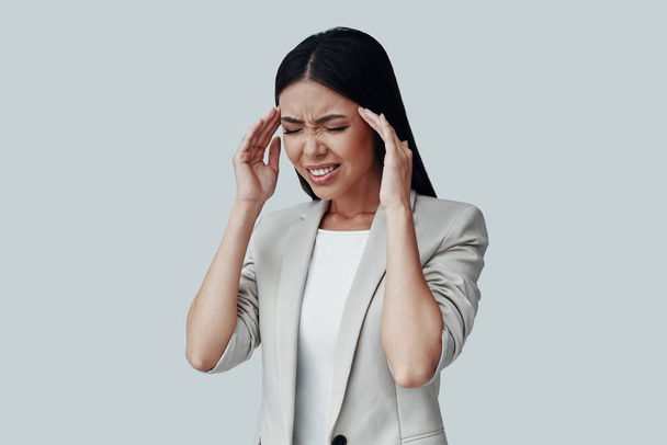 Sentir el dolor. Frustrado joven mujer asiática haciendo una cara, mientras que de pie sobre fondo gris
 - Foto, Imagen