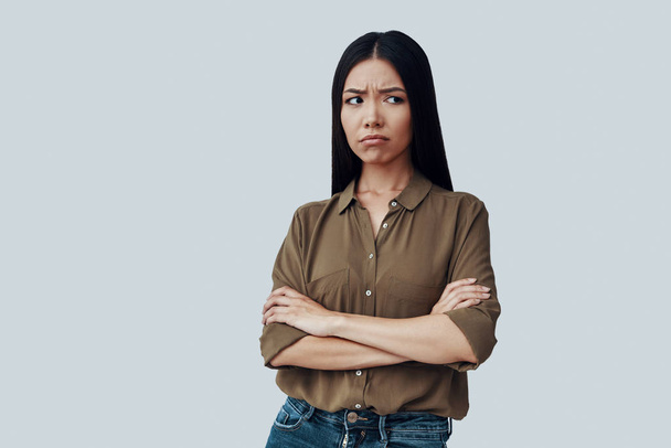 What can I do? Confused young Asian woman making a face while standing against grey background - Photo, Image