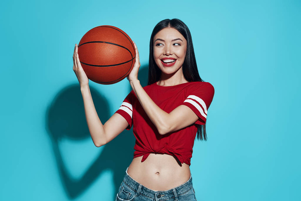 Jogo favorito. Atraente jovem mulher asiática sorrindo enquanto está de pé contra o fundo azul
 - Foto, Imagem