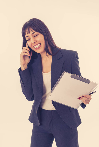 Close up of a young beautiful business woman standing speaking on the phone holding a folder. Smiling feeling confident and successful. In people business education, communication and work concept. - Fotoğraf, Görsel