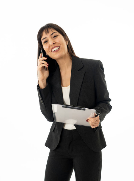 Close up of a young beautiful business woman standing speaking on the phone holding a folder. Smiling feeling confident and successful. In people business education, communication and work concept. - Photo, Image