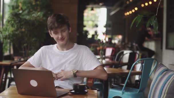 junger europäischer Mann, der im Café lächelt und lacht, Freiberufler und Blogger, der sich im Café lustig unterhält, moderne Kommunikation durch Online-Verbindung im Café. Laptop im Restaurant geöffnet. - Filmmaterial, Video