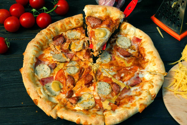 Cut off pizza, on slices, with sausage, tomato and cheese. On wo - Photo, Image