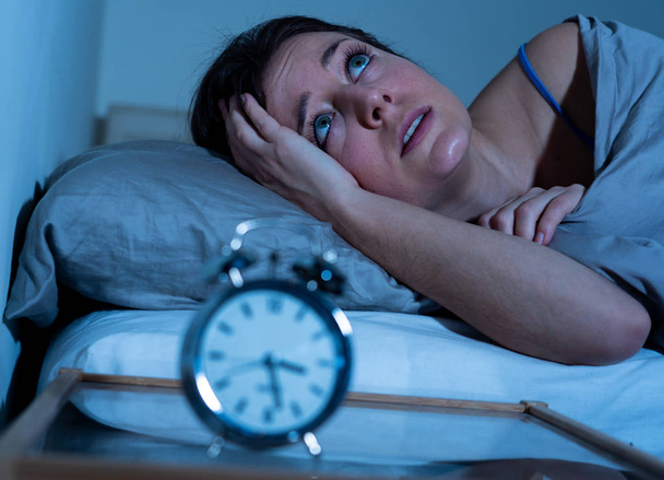 Sleepless and desperate beautiful caucasian woman awake at night not able to sleep, feeling frustrated and worried looking at clock suffering from insomnia in sleep disorder concept. - Foto, Imagem