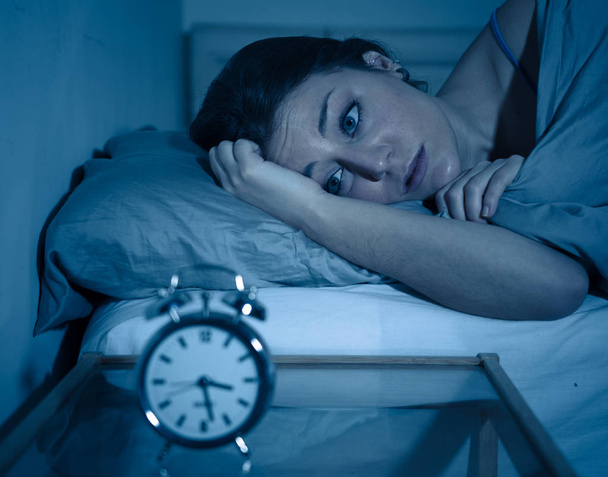 Slapeloze en wanhopig mooie Kaukasische vrouw wakker in de nacht niet kunnen slapen, gevoel gefrustreerd en bezorgd over het lijden aan slapeloosheid in slaap stoornis concept klok kijken. - Foto, afbeelding