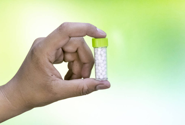 Człowiek trzyma butelkę homeopatycznych pigułki na mix zielone żółte tło. Medycyna i leczenie - Zdjęcie, obraz
