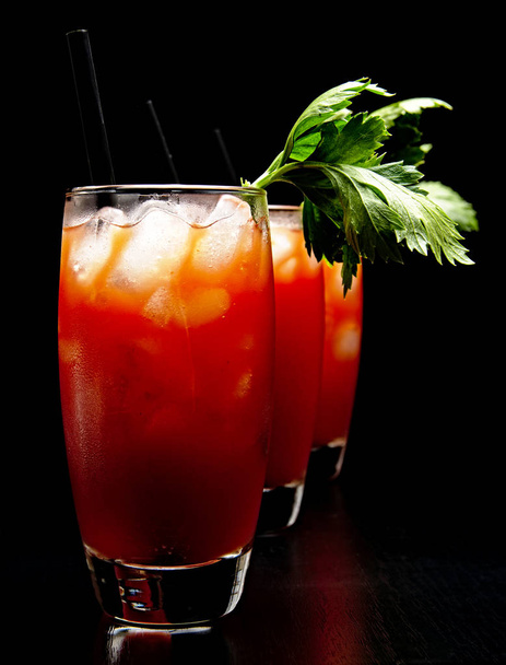 Bloody Mary cocktails with ice cubes and celery on black - Foto, Imagen