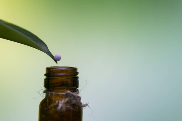 Homeopathic pill on the tip of a leaf rolling down in the bottle with green yellow background. - Photo, Image