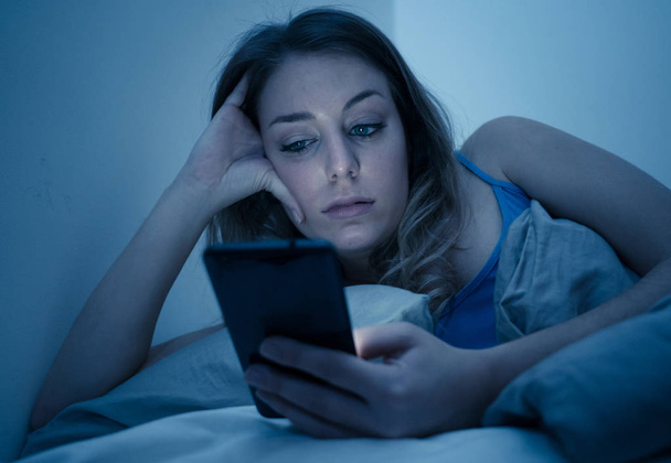 Addicted young beautiful woman in bed, chatting and surfing on the internet using her smart phone sleepy, dull and tired late at night in mobile addiction and technology overuse concept. - Photo, Image