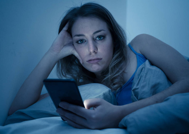 Addicted young beautiful woman in bed, chatting and surfing on the internet using her smart phone sleepy, dull and tired late at night in mobile addiction and technology overuse concept. - Foto, Bild