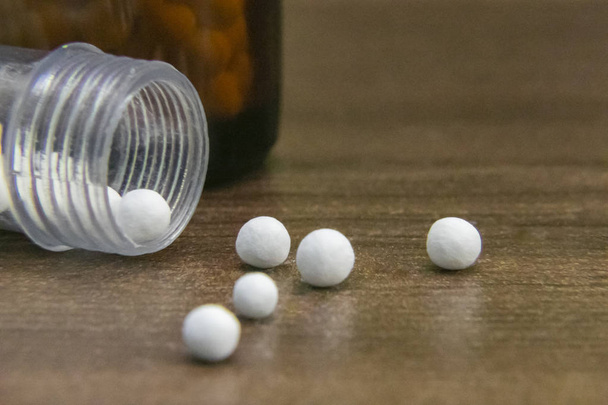 Close View beeld van verspreide homeopathische bolletjes en fles op houten achtergrond. Homeopathie geneeskunde - Foto, afbeelding