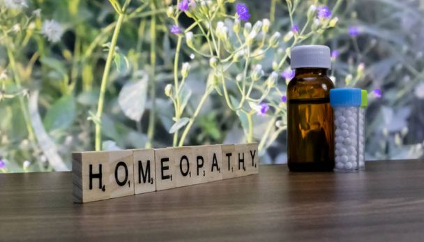 Бутылки гомеопатической медицины на деревянной поверхности с диким цветочным фоном и наклонным текстом гомеопатии на столе
. - Фото, изображение
