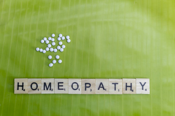 Natural Homeopathic Concept - Scattered Homeopathic medicine pills on banana leaf with Homeopathy text - Photo, Image
