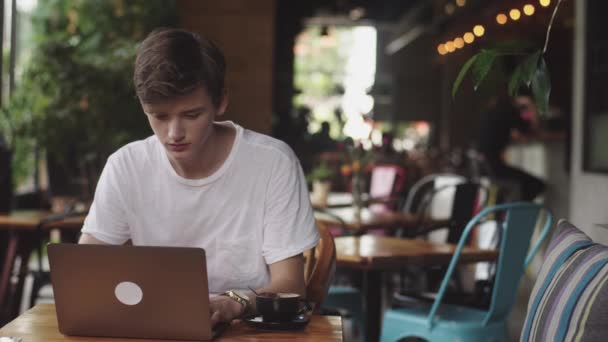 Młody człowiek kończy pracę, freelancer i blogger pracy jako projektant graficzny kryty, nowoczesne miejsce pracy siedzi w kawiarni. Otwórz laptopa w restauracji. - Materiał filmowy, wideo