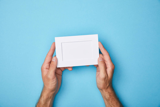 cropped view of man holding white empty card in frame on blue background - Foto, afbeelding