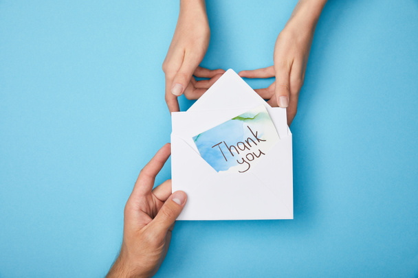 przycięte widok człowieka dając kartkę z życzeniami dziękuję napis w kopercie do kobiety na niebieskim tle - Zdjęcie, obraz