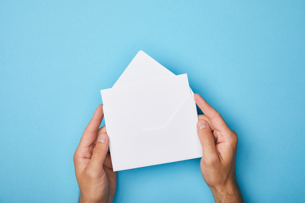 cropped view of man holding envelope with blank white card on blue background - Foto, Imagen